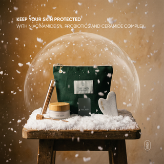 Cosmetic products including a cosmetic pouch, moisturizer jar, affirmation card and sandalwood incense and gua sha on a wooden stool with snow effect and 'THY SKIN' branding.