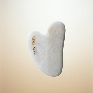 White gua sha tool with 'The Skin' branding on a beige background